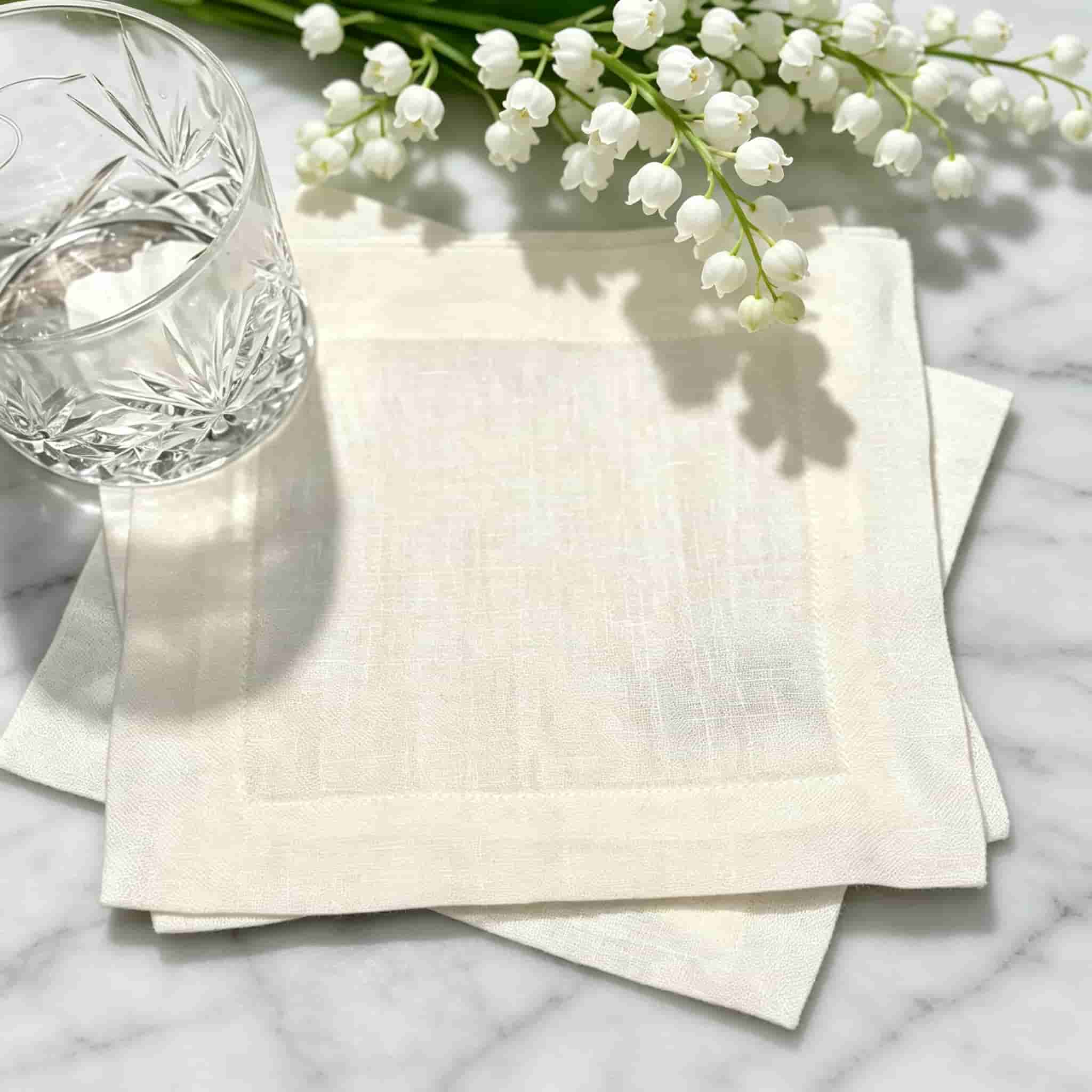 Ivory pure linen cocktail napkin with monogram embroidery beneath crystal rocks glass on luxury bar surface