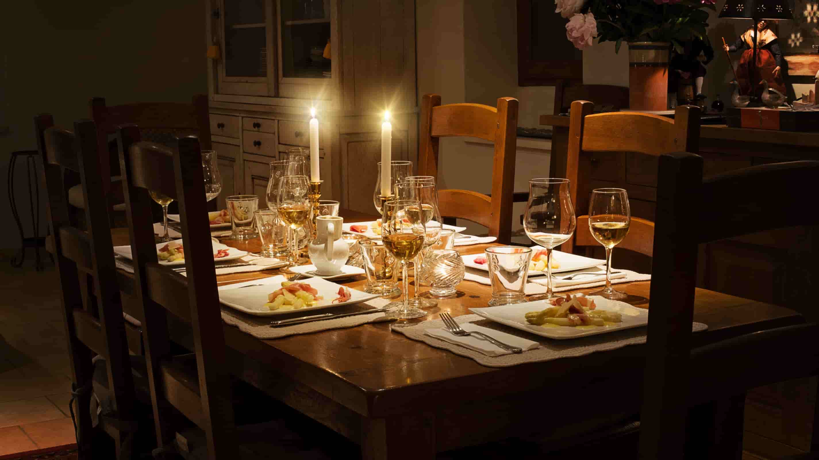 Washed linen placemats on a rustic farmhouse dining table set for six with crystal wine glasses and white taper candles