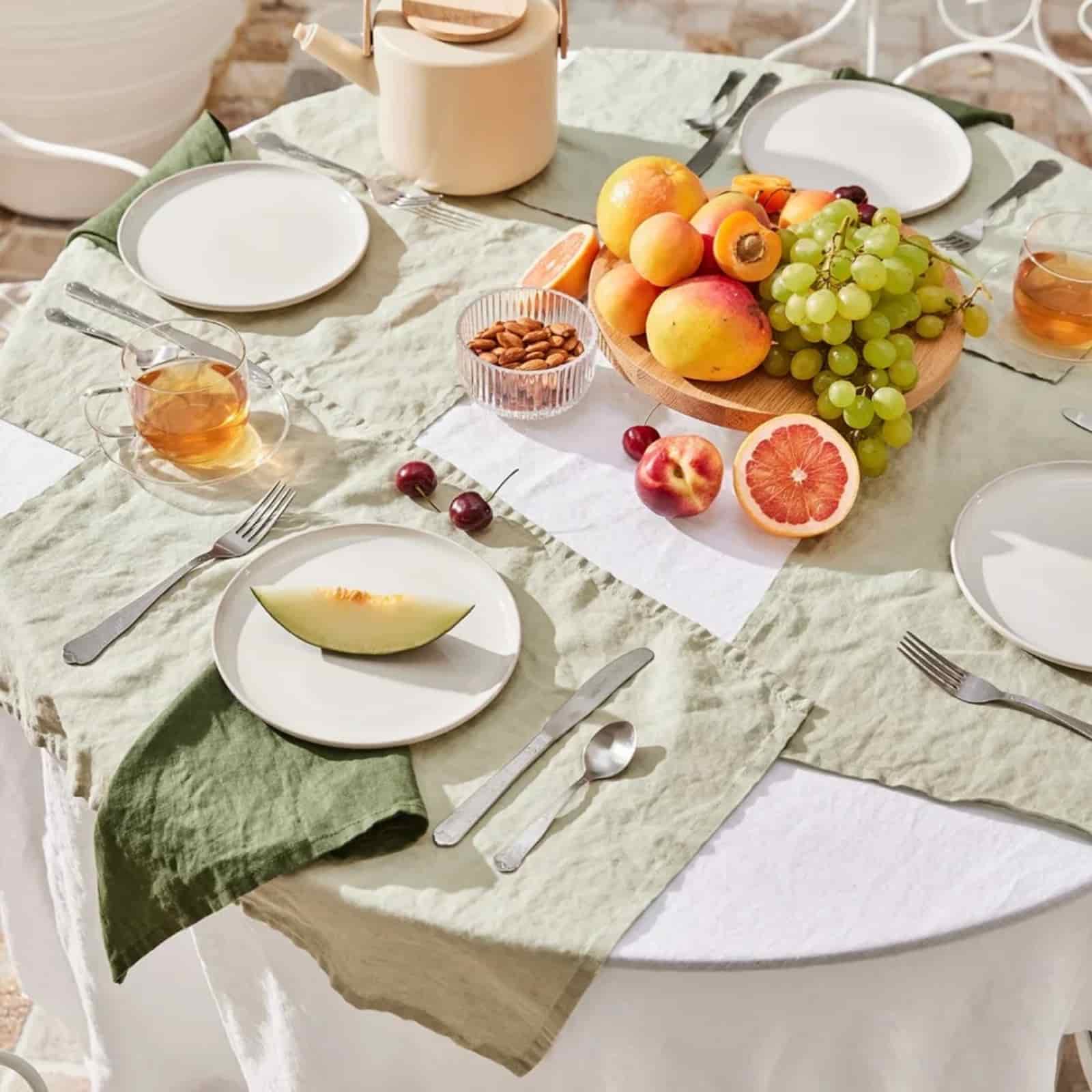 Sage green linen placemat on outdoor round table with fruit brunch