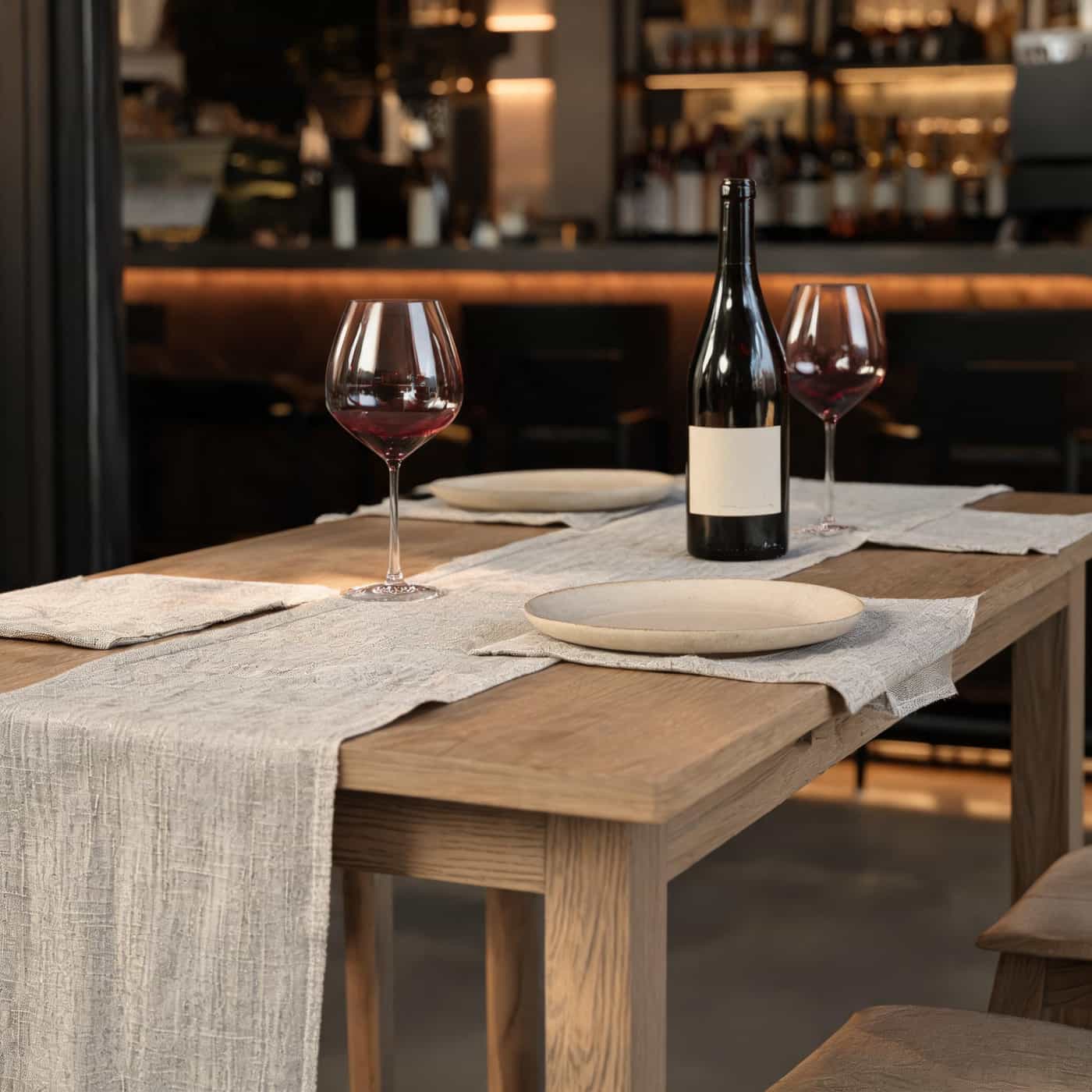 Natural linen placemats and table runner styled with red wine glasses and bottle in a warm restaurant setting