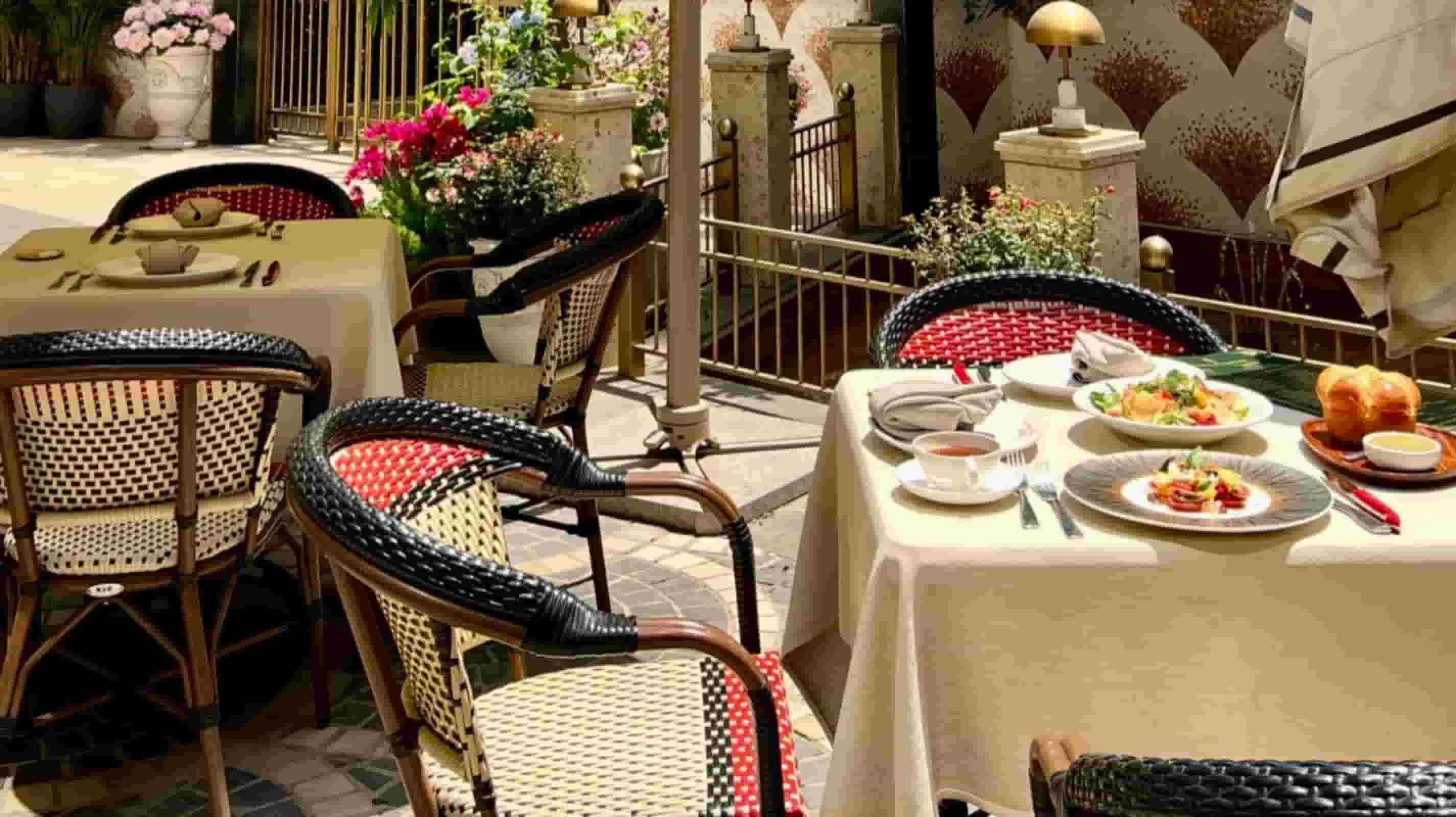 Beige linen tablecloths on rattan bistro chairs at a sunlit Mediterranean hotel courtyard terrace with bougainvillea and served breakfast plates
