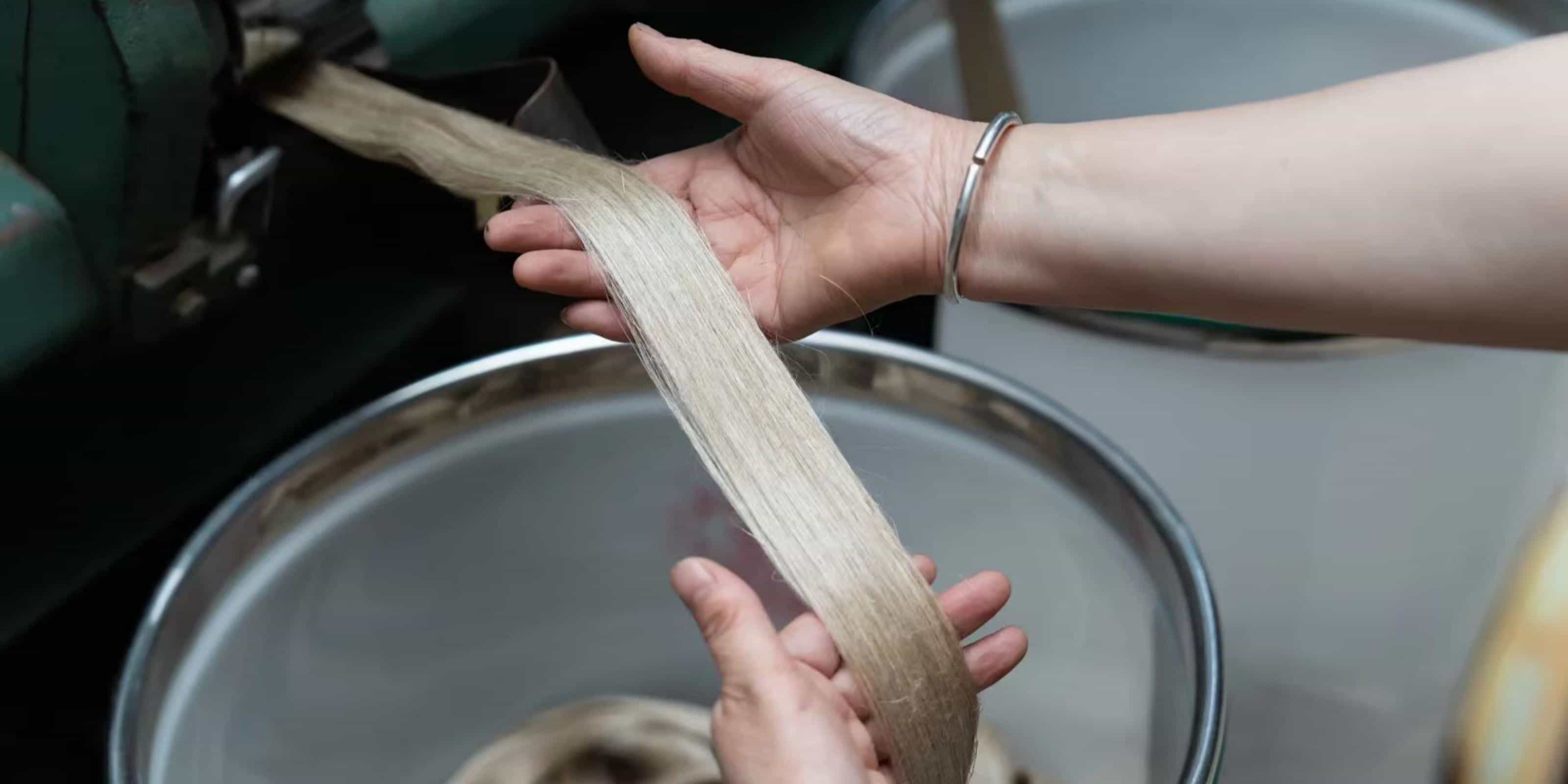 Hands inspecting raw linen fiber material for quality control at Budloop textile factory