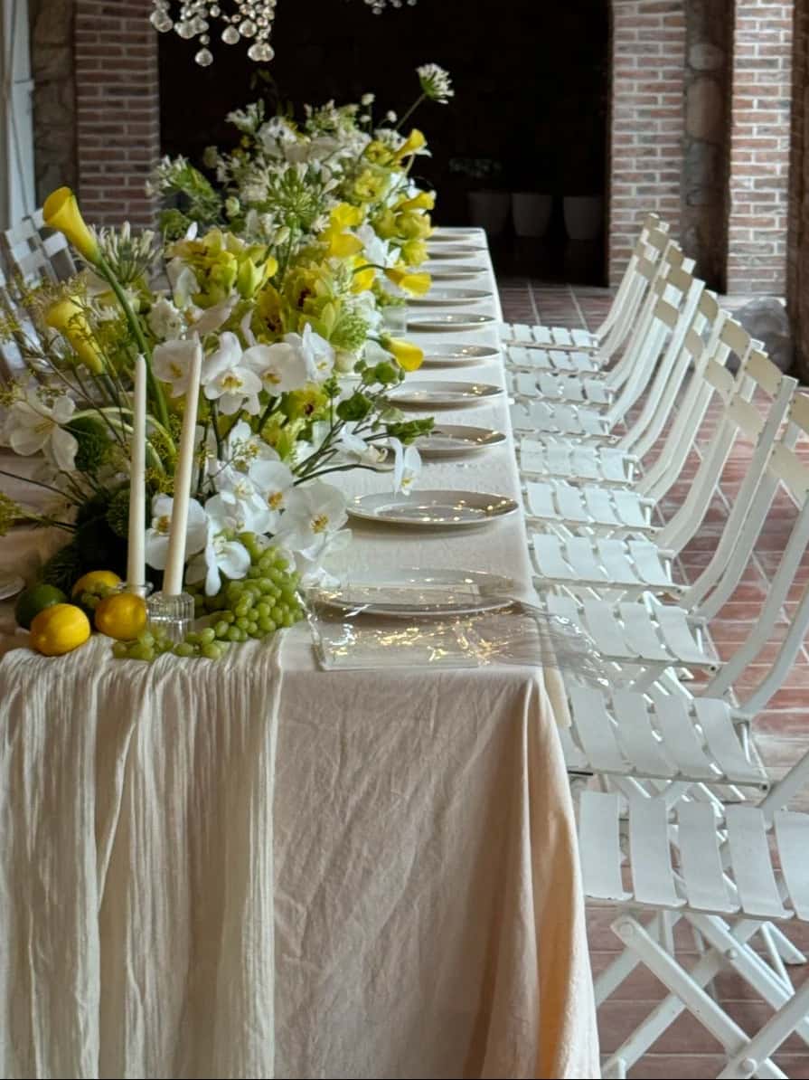 Outdoor banquet long table with white linen tablecloth, yellow and white floral centerpieces and white chairs