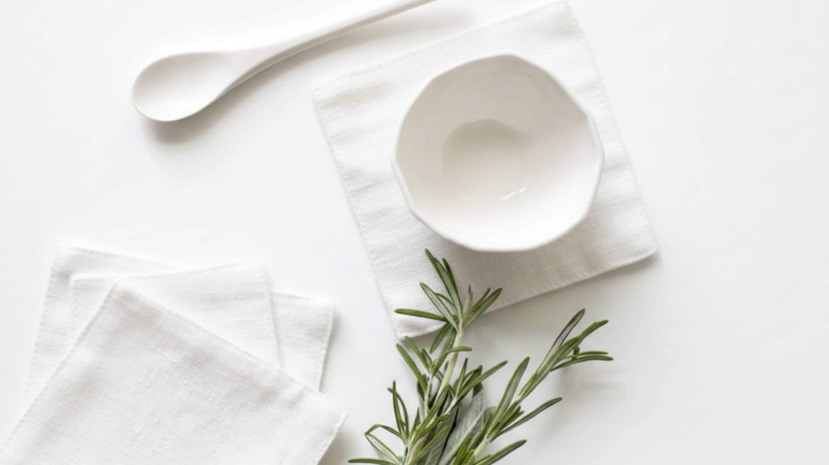 White washed linen coasters with white ceramic bowl, spoon and fresh rosemary on white background, flat lay