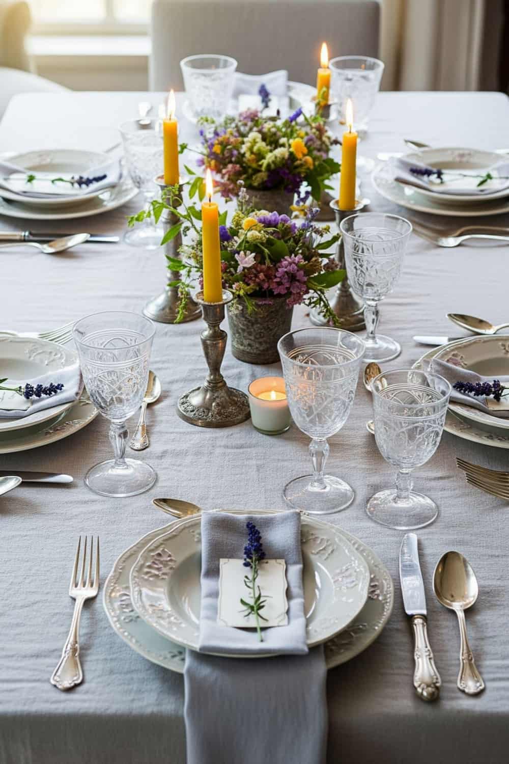 An editorial fine dining table setup featuring luxury grey linen table linens, lit yellow candles, crystal stemware, and wildflowers, showcasing reliable wholesale contract textile scaling for hospitality buyers.