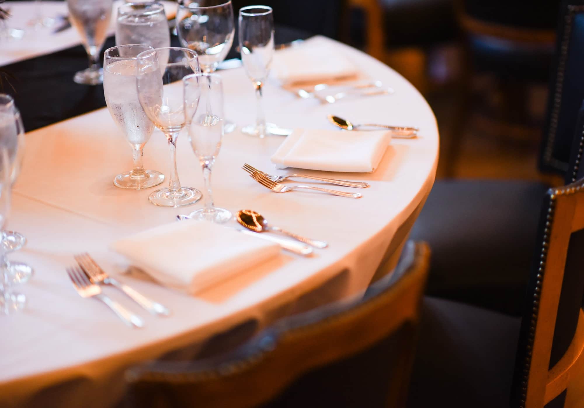 Close-up of a fine dining round table with white linen napkins, polished silverware, and crystal glassware in a dark upscale restaurant