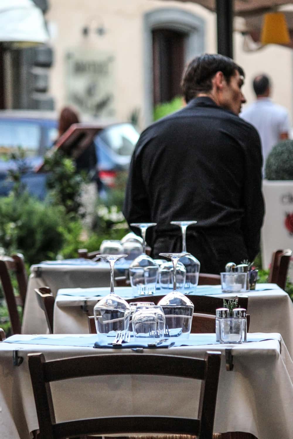 Neutral linen tablecloths and blue linen napkins on outdoor bistro tables at an Italian street-side restaurant terrace