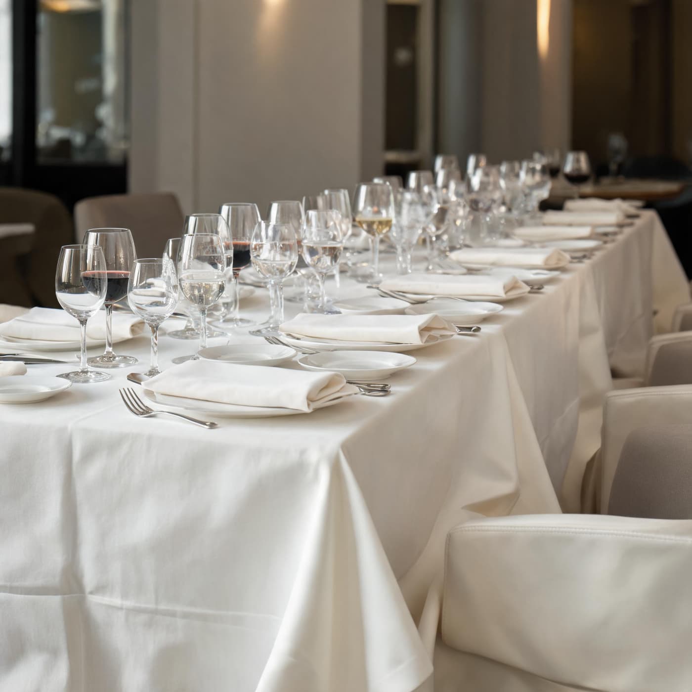 Formal fine dining banquet table with white linen tablecloths, folded napkins, and multiple wine glasses