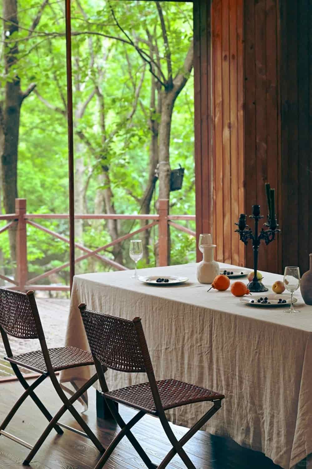 Softly wrinkled washed linen tablecloth on a dining table inside a wooden cabin overlooking a lush green forest