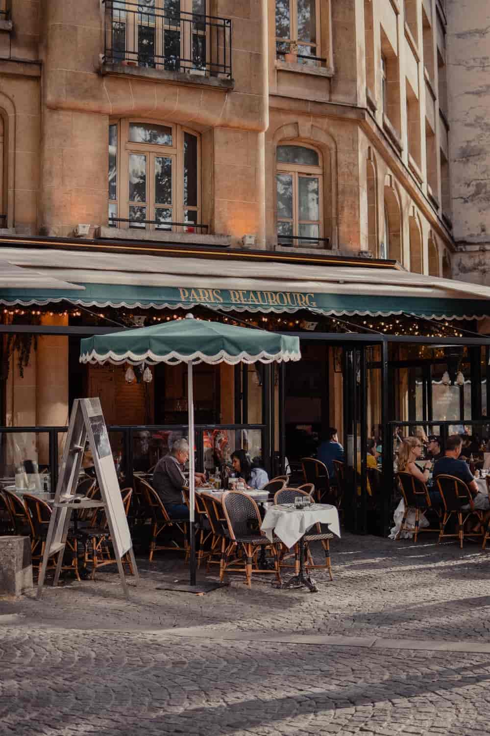 White linen tablecloths on wicker bistro chairs outside a classic Parisian sidewalk café on a cobblestone street at golden hour